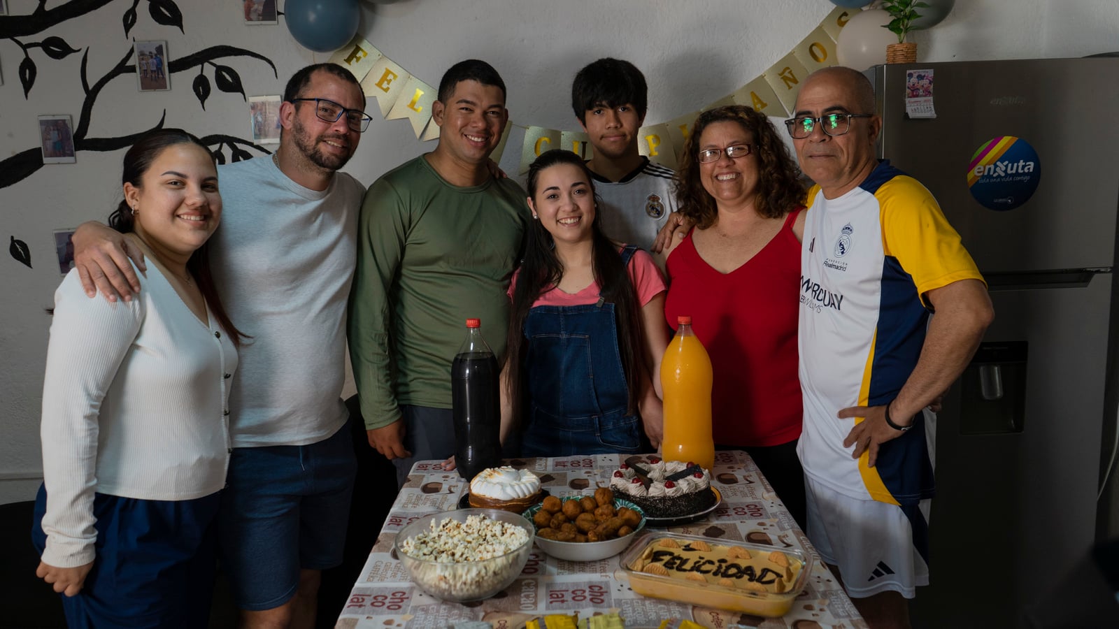 Tres hombres, tres mujeres y un adolescente celebran un cumpleaños en la cocina de una casa