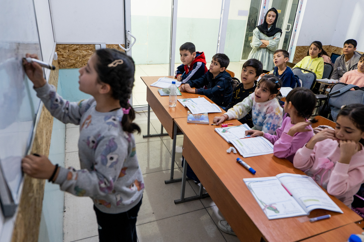 Una niña escribe en una pizarra blanca frente a una clase de niños