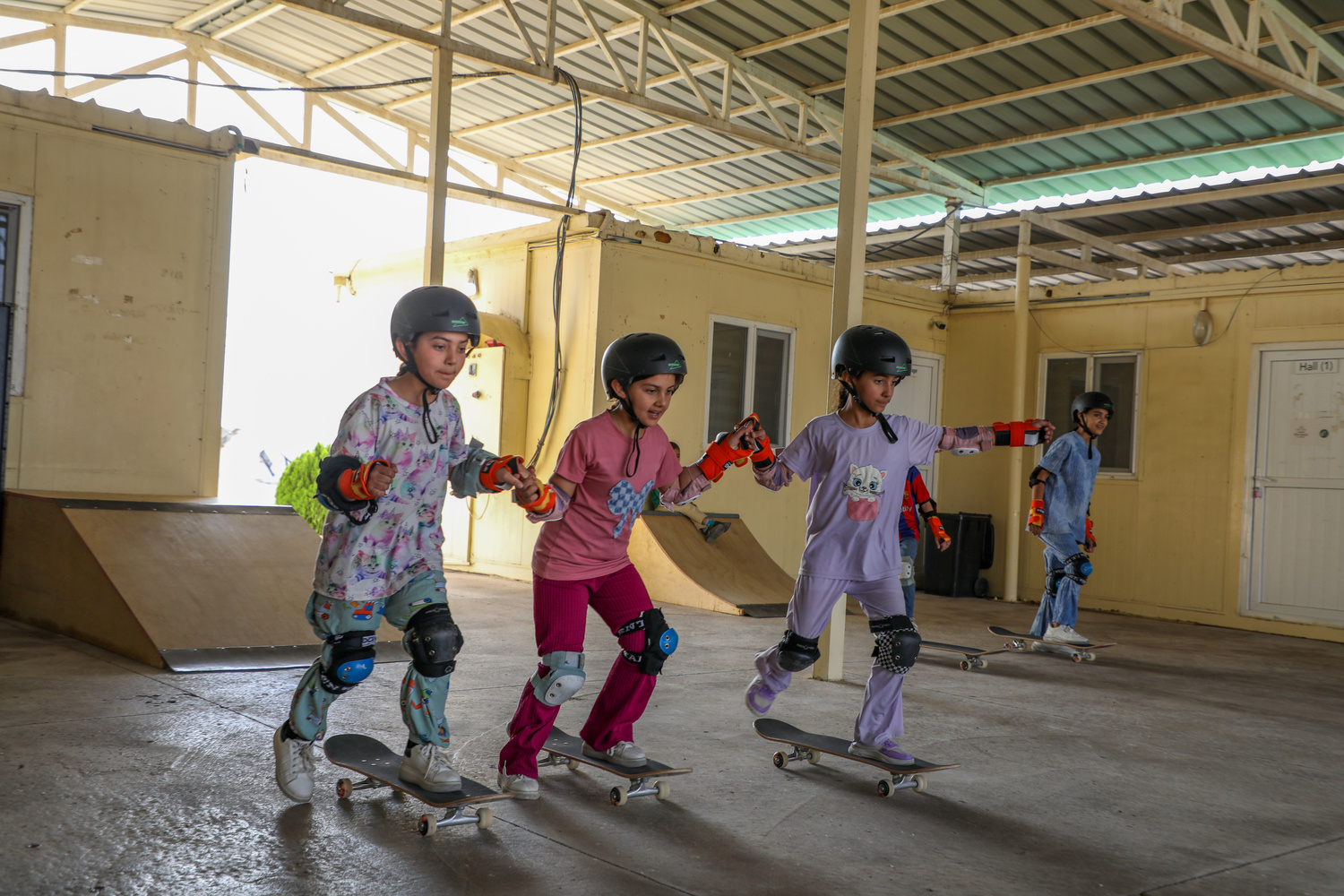 Niñas con equipo de protección sobre patinetas dentro de un gran edificio