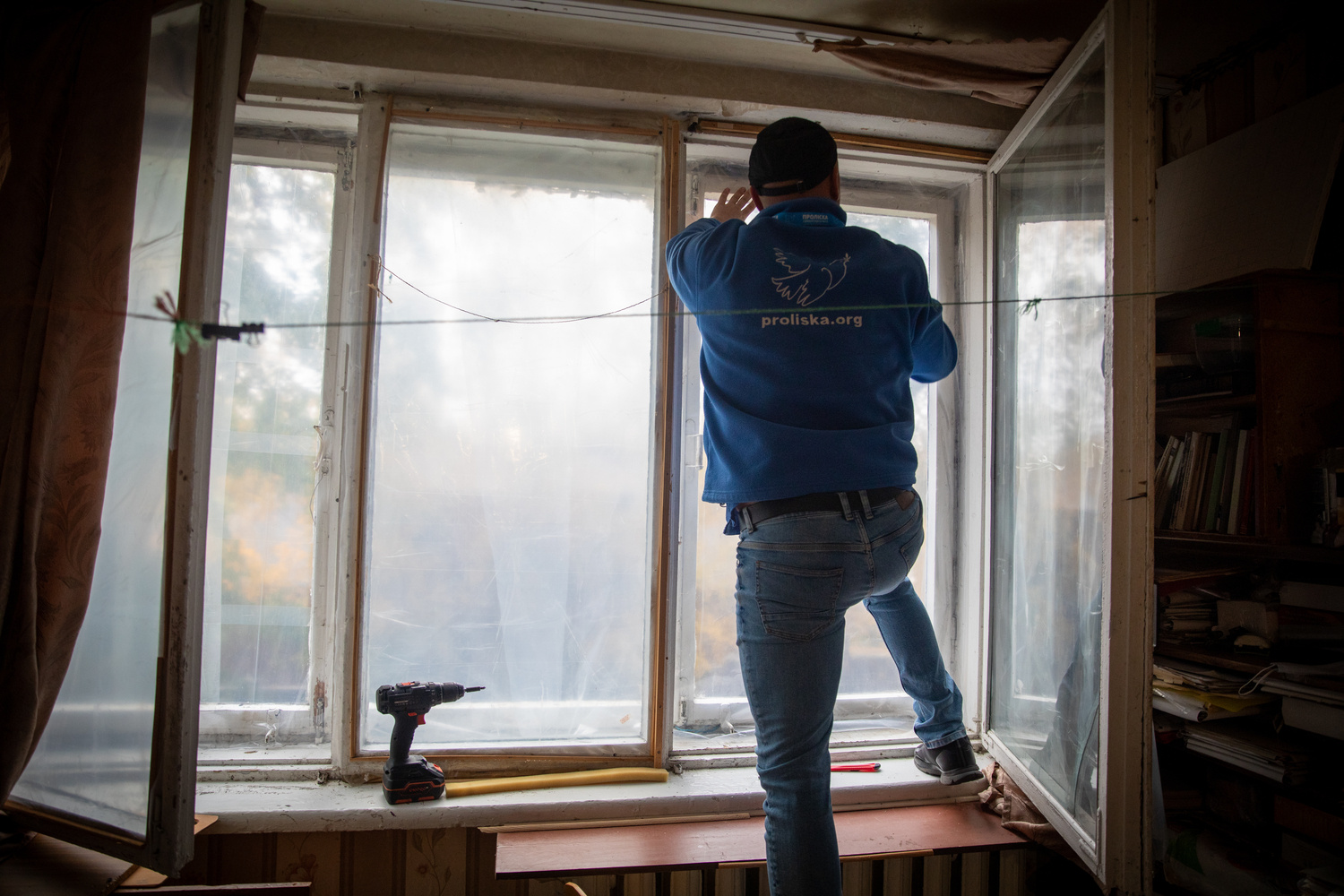 Un hombre se sube al borde de una ventana interior para realizar reparaciones