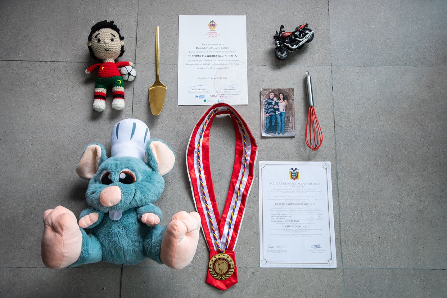 Objetos personales ordenados sobre una superficie: hay peluches, títulos de grado, una foto, una medalla, entre otros.
