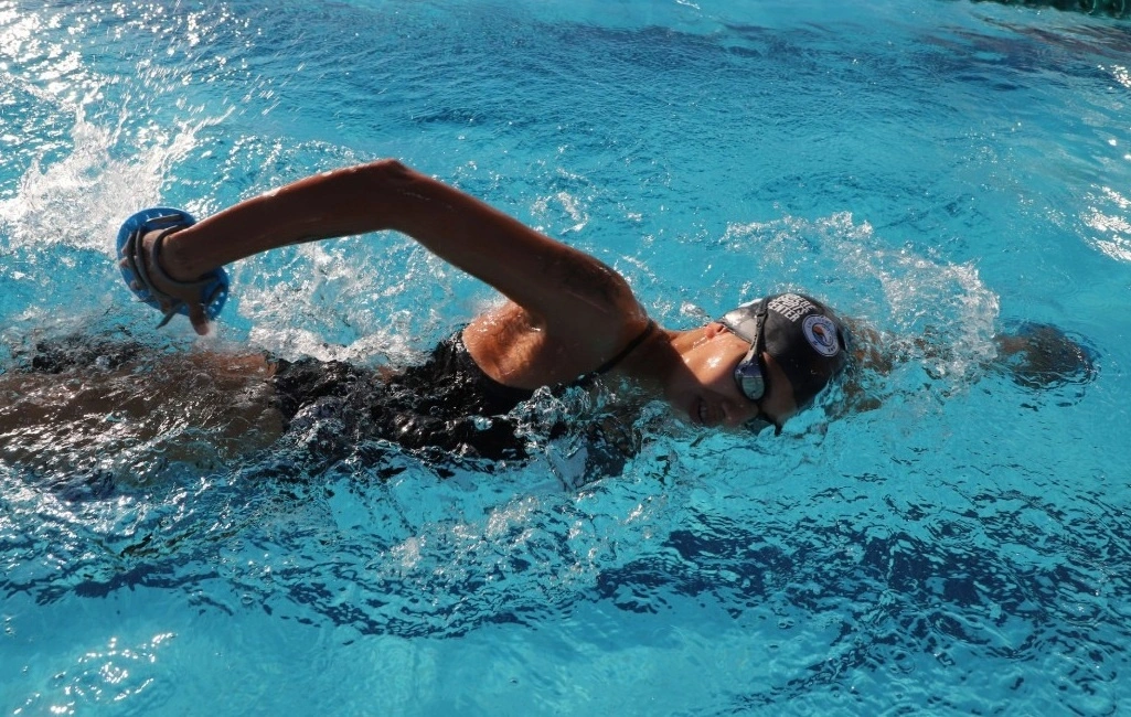 Una mujer nada en una alberca con traje de baño, gorra de natación y googles