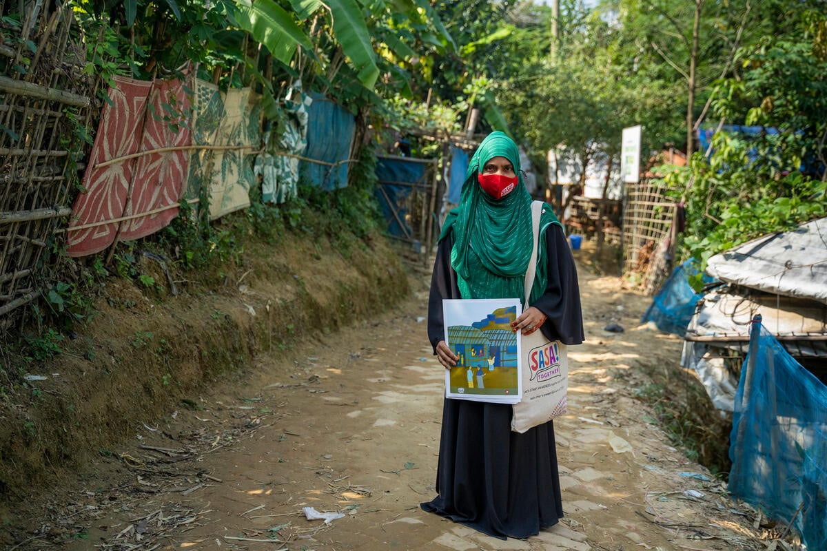 En medio de un camino, una mujer, que lleva el rostro y la cabeza cubiertos con un hiyab, muestra un dibujo y mira fijamente a la cámara.