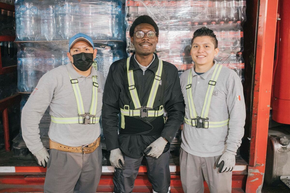 Tres hombres posan para la foto delante de un camión cargado de cajas de bebidas.