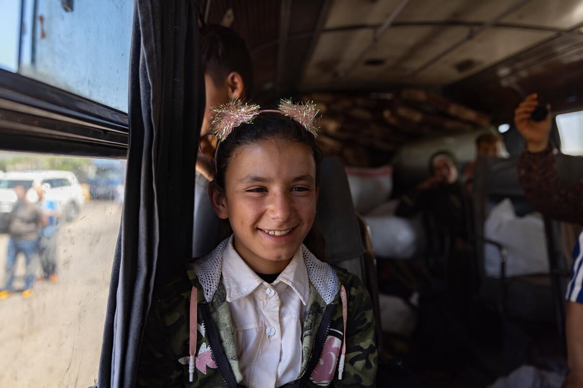 Una niña sonriente sentada junto a la ventanilla de un autobús