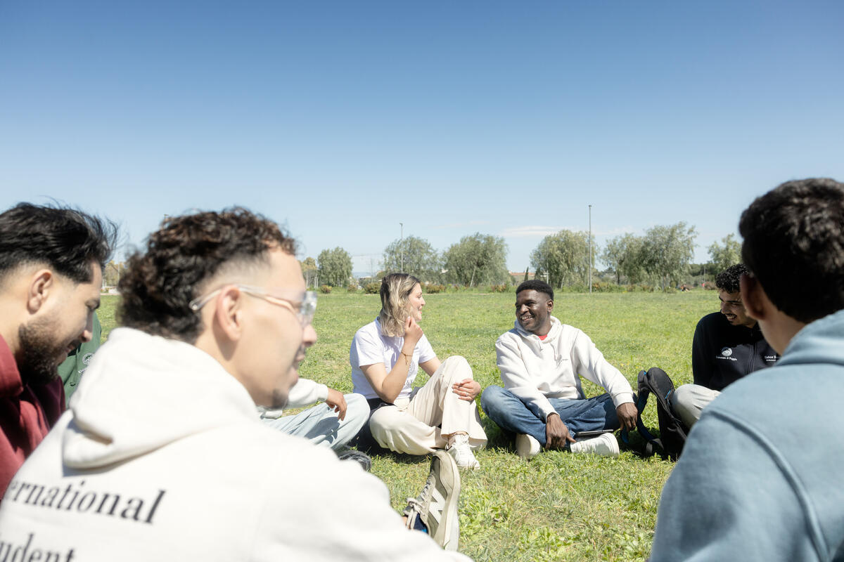 Un grupo de jóvenes hablando sentados en el césped en un parque.