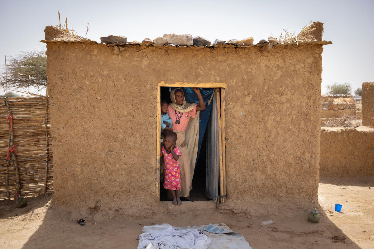 Una madre posa con sus dos hijos en la entrada abierta de una pequeña casa de adobe