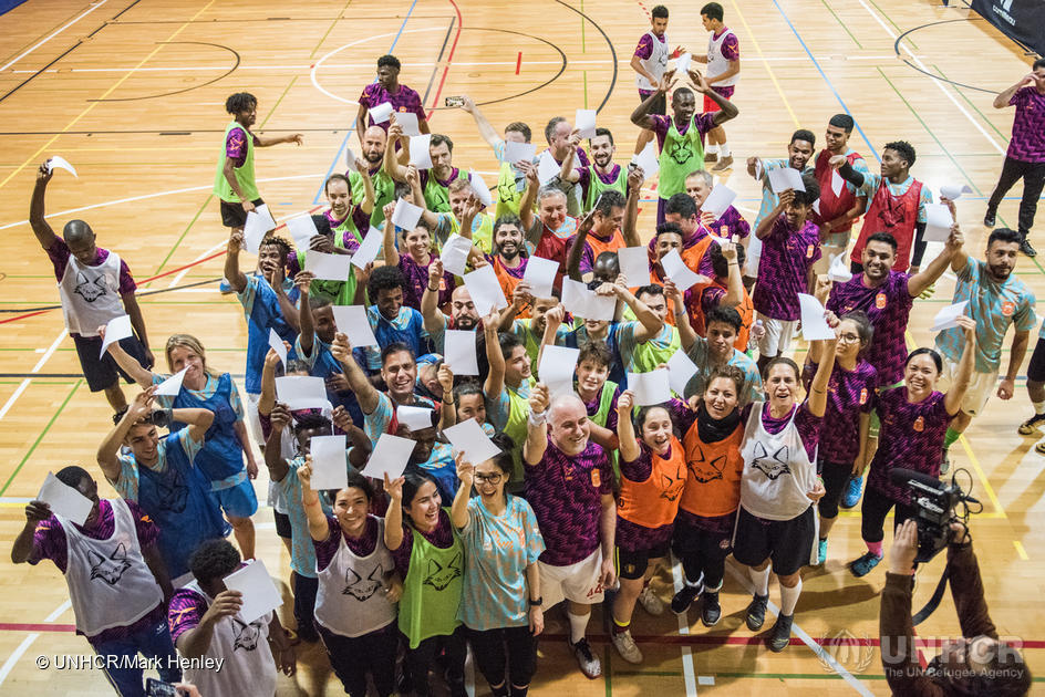 Un grupo de personas vestidas con ropa deportiva saluda a la cámara desde una cancha de baloncesto