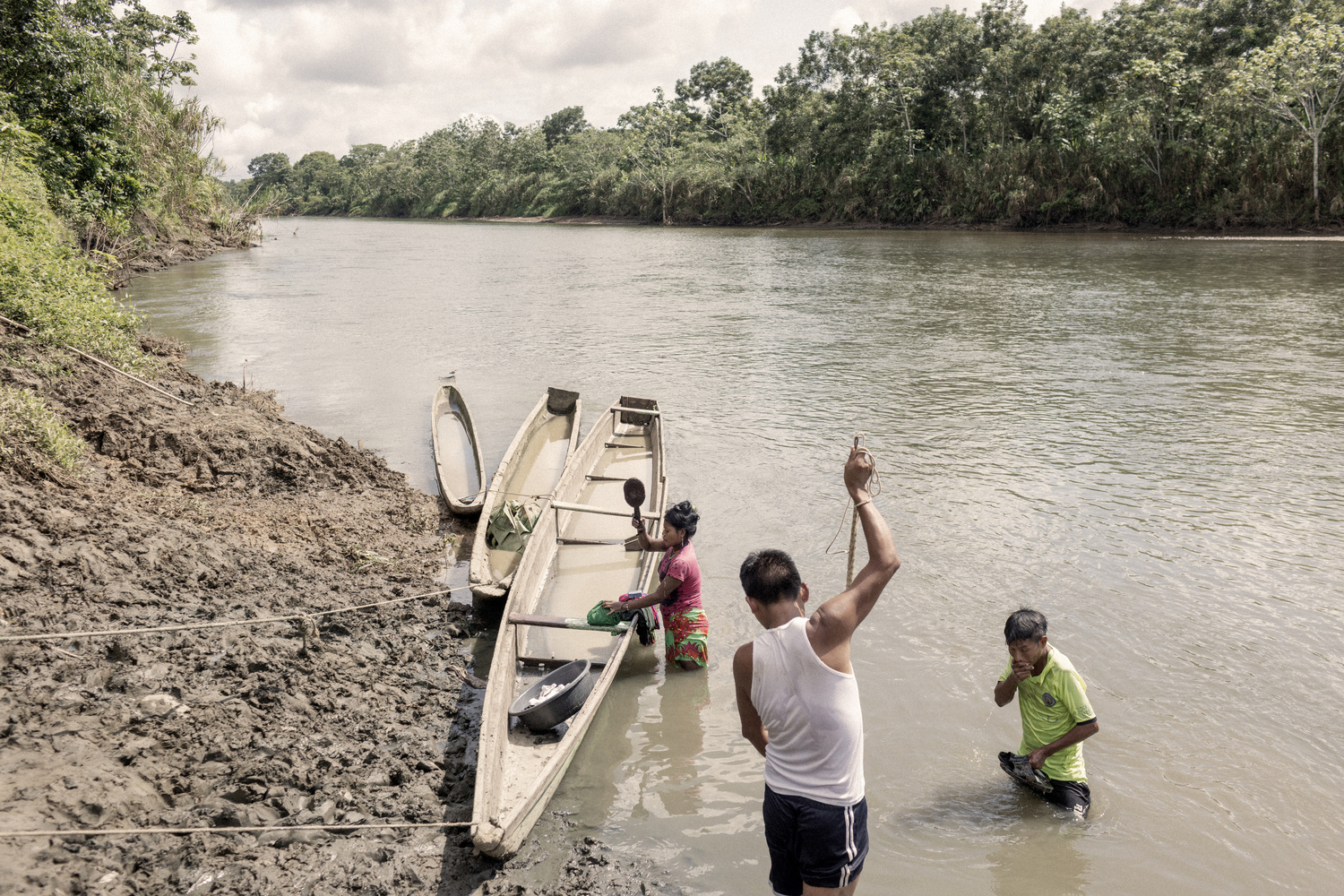 Tres personas en un río: una mujer que lava ropa, un hombre que se asea y otro hombre que prepara redes de pesca