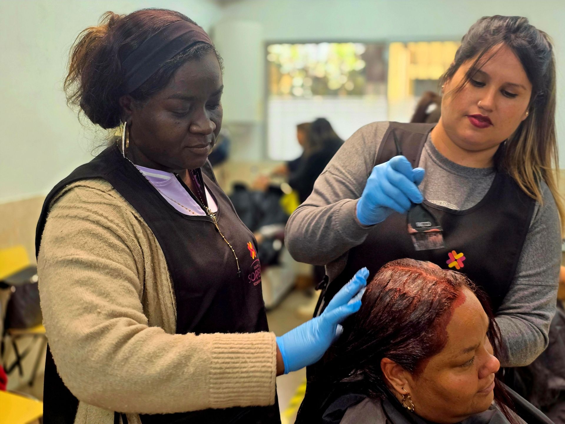 Dos mujeres le ti&ntilde;en el pelo a una clienta en una peluquer&iacute;a.