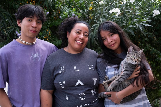 Al centro, una mujer con su hija y su hijo adolescentes. Su hija, quienestá a su lado izquierdo, sostiene entre sus brazos a un gato