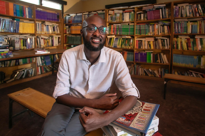 Un hombre somalí que usa anteojos sonríe a la cámara, sentado en una biblioteca