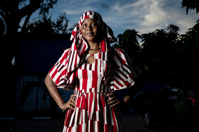 Una mujer de Burkina Faso, que lleva puesta una indumentaria a rayas color rojo y blanco, ve fijamente a la cámara con los brazos puestos sobre la cadera
