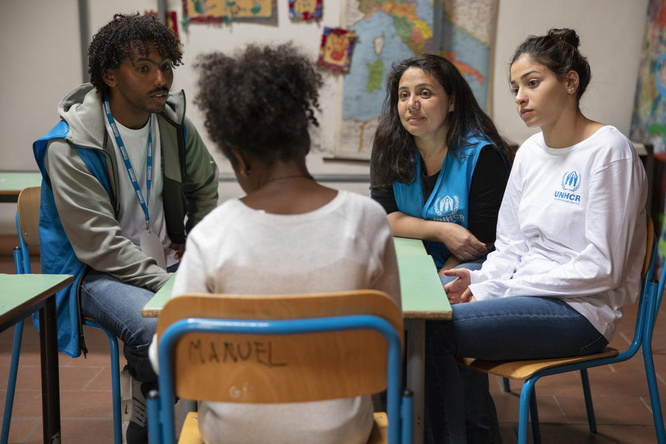 Tres mujeres y un hombre conversan; están sentados en un pequeño círculo en lo que parece un aula.