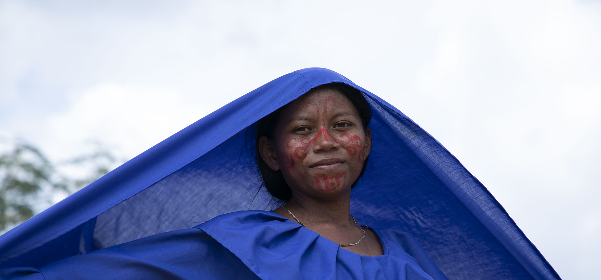 Una mujer indígena vestida de azul mantiene un velo azul sobre su cabeza.