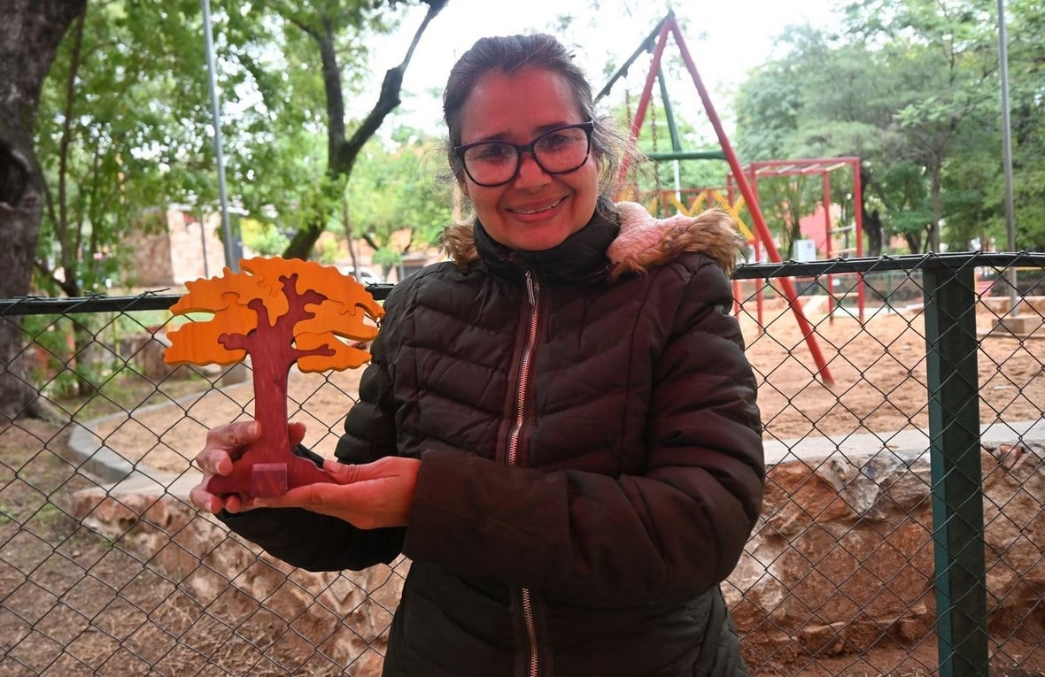 Una mujer posa frente a cámara mostrando un árbol de madera tallada.