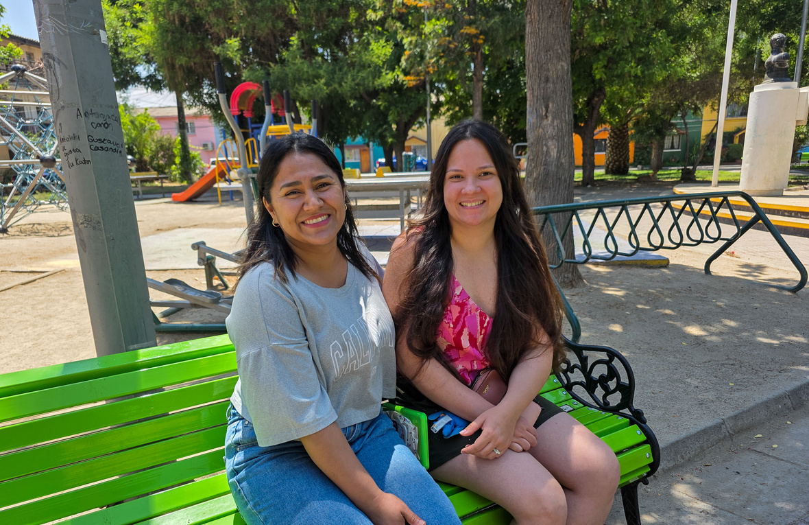 Dos mujeres jóvenes posan para la foto, de pie en un parque con árboles al fondo