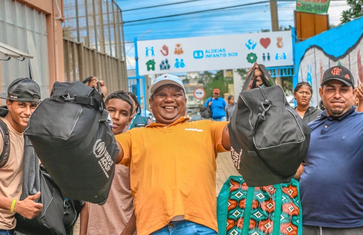 Un grupo de personas posa para la foto en la calle con al centro un hombre que muestra dos maletas sonriendo.