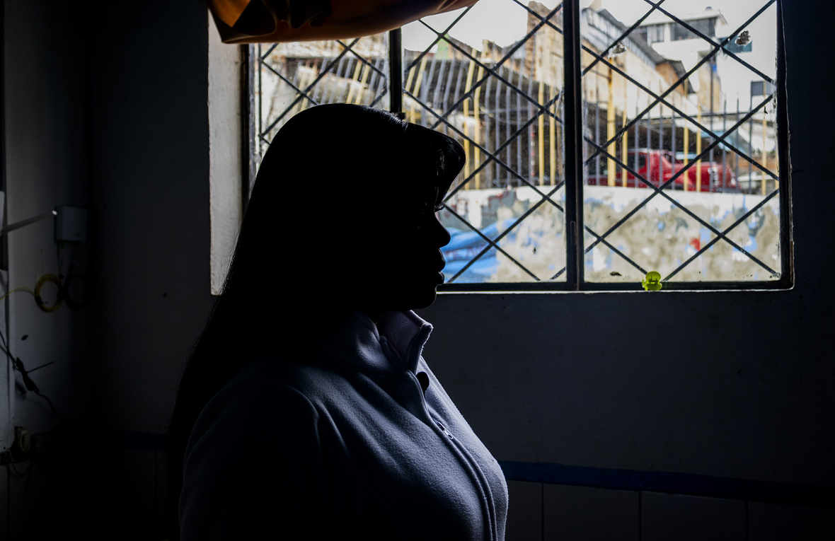 Una mujer fotografiada de perfil y contraluz mira a través de una ventana.
