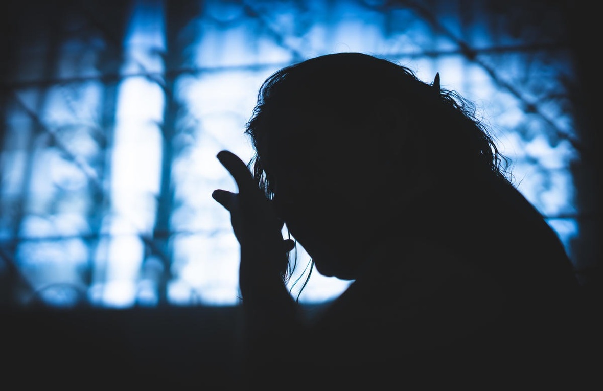 Silueta de una mujer a contraluz en una ventana que refleja luz azul