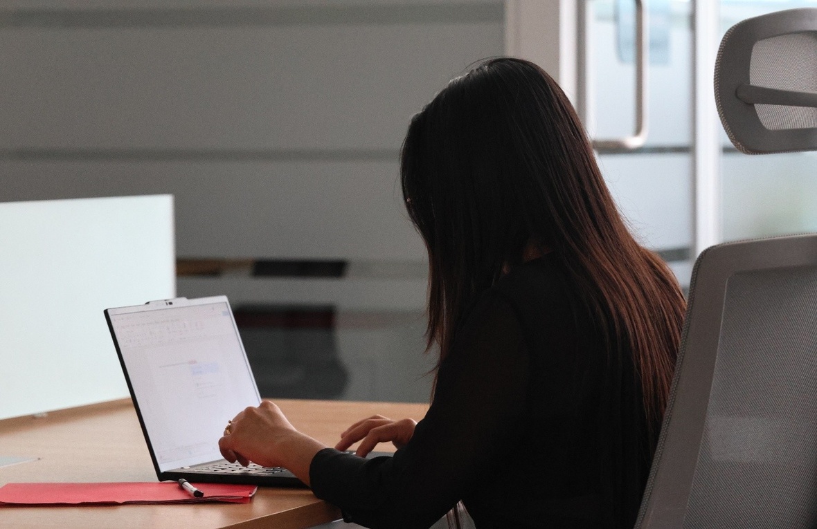 Una mujer de espaldas escribiendo en una computadora.