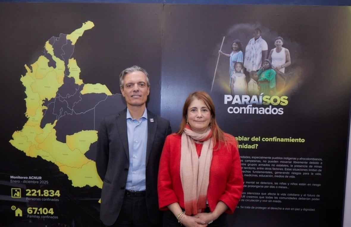 Un hombre y una mujer posan para la cámara delante de un cartel con el mapa de Colombia y el afice de la exposición Paraísos Confinados.