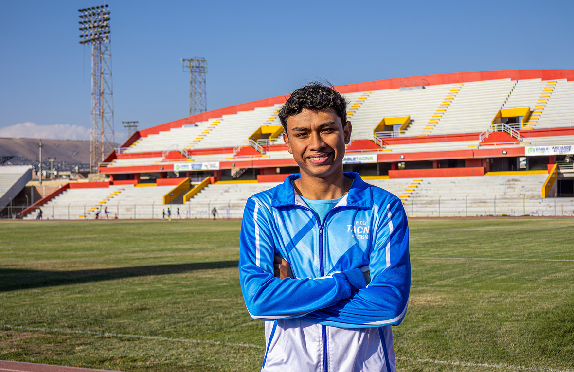 Un joven con uniforme deportivo azul claro con blanco, posa cruzado de brazos de pie en una pista de atletismo
