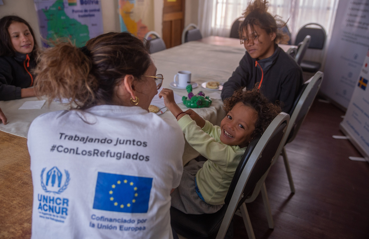 Sentados a la mesa con alimentos se encuentran dos mujeres, una joven y un niño sonriente