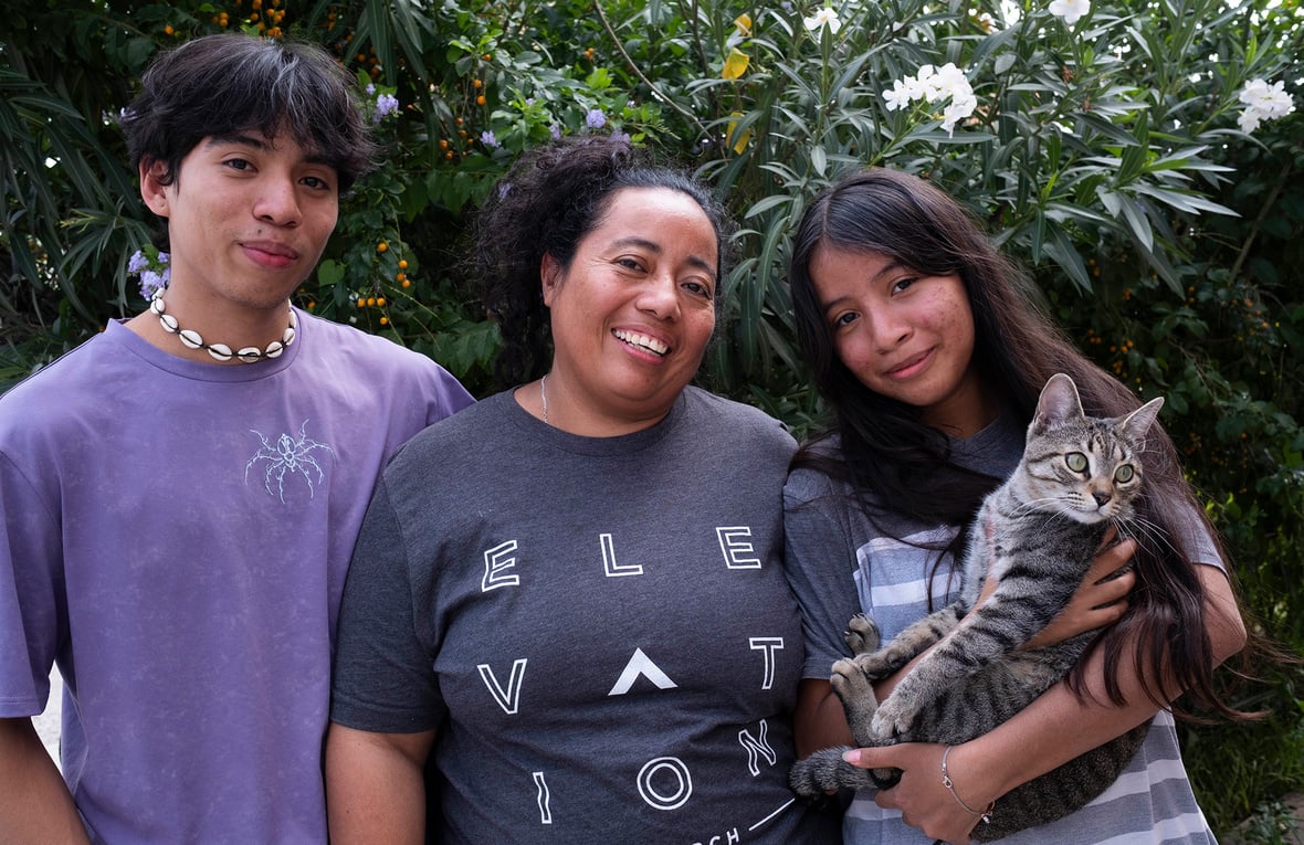 Al centro, una mujer con su hija y su hijo adolescentes. Su hija, quienestá a su lado izquierdo, sostiene entre sus brazos a un gato