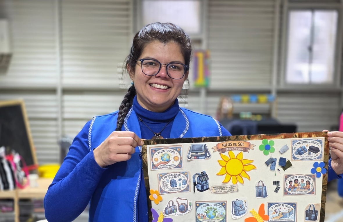 Una mujer con camiseta manga larga azul y chaleco azul, sostiene un tablero con recortes coloridos