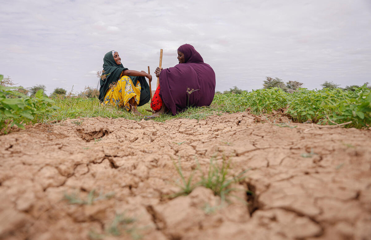 Dos mujeres con la cabeza cubierta platican mientras están sentadas en la tierra