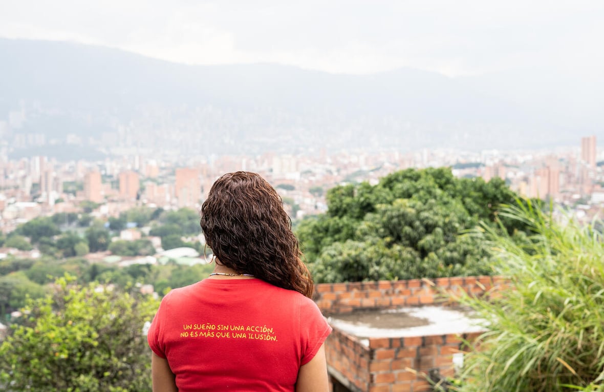 Una mujer de espaldas mirando a un paisaje urbano desde un mirador.