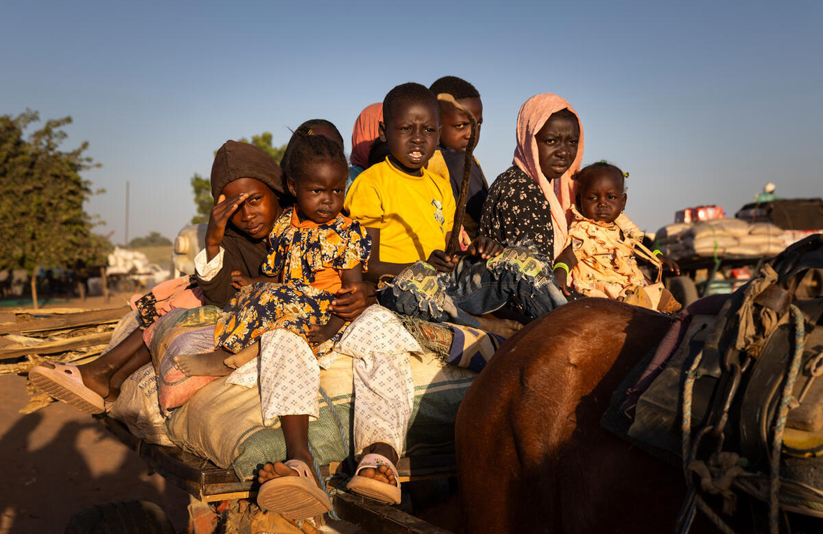 Un grupo de niños sudaneses sentados encima de un auto detrás de un caballo