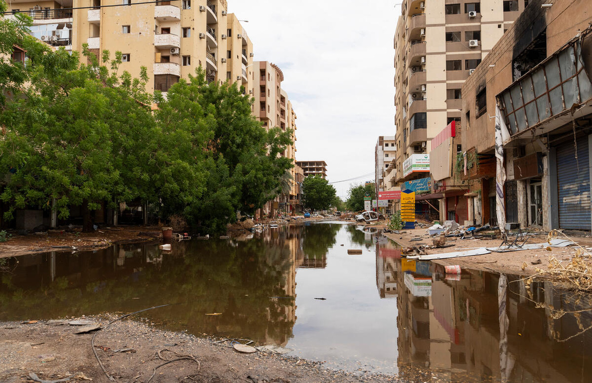Vista de una calle despavimentada e inundada rodeada de edificios y escombros.