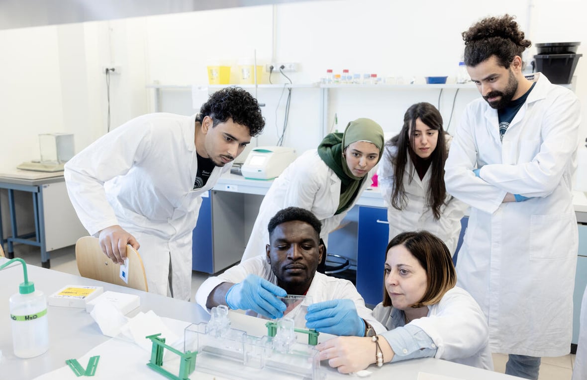 Un grupo de estudiates en bata médica haciendo pruebas en un laboratorio.