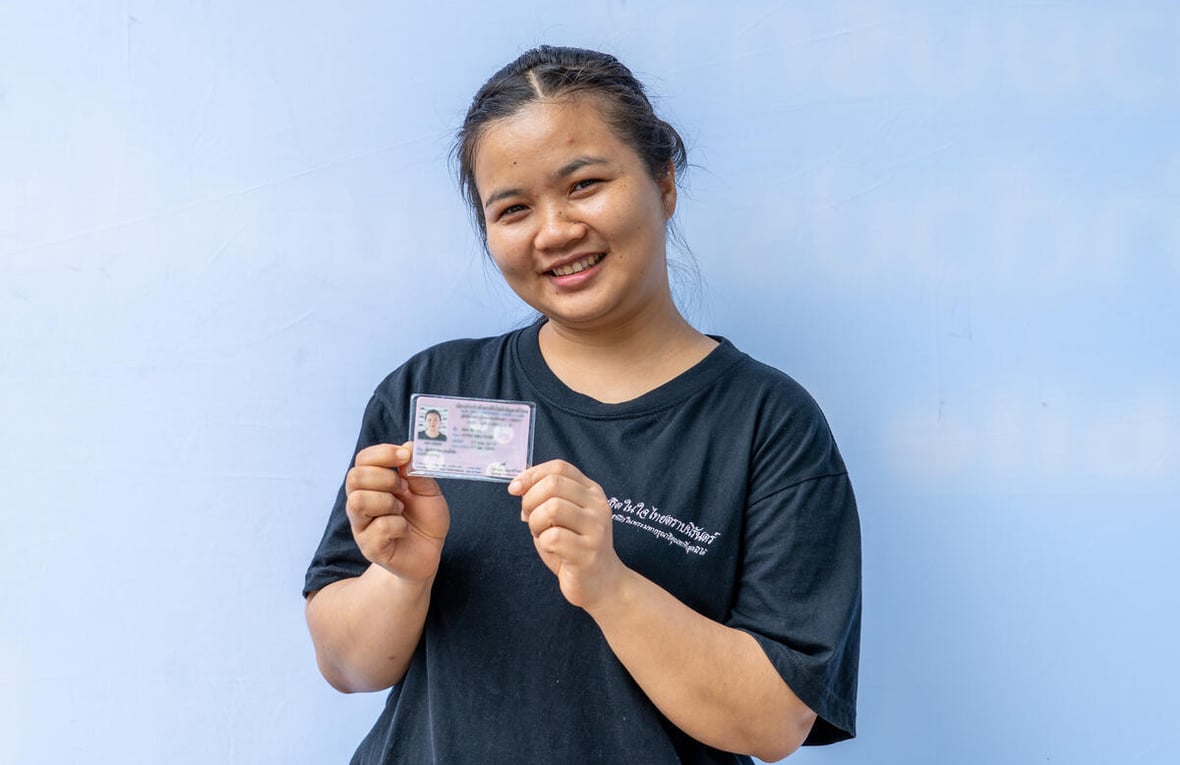 Una joven sonriente que viste una camiseta negra sostiene con sus dos manos un documento de identidad