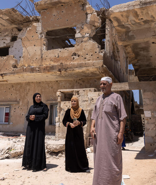 Siria. Un grupo de personas de pie delante de los escombros de una vivienda dañada por bombardeos.