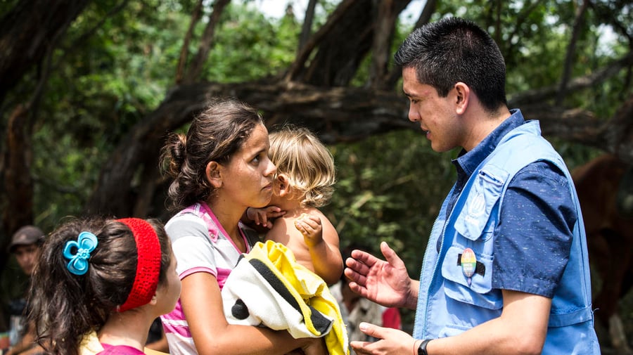 Una mujer con dos niños pequeños charla con un trabajador de ACNUR en Colombia.