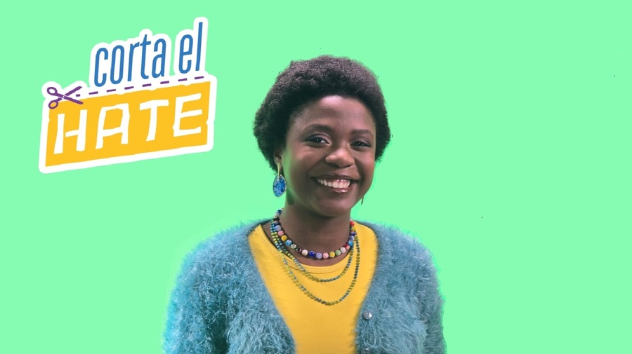 Una mujer que viste suéter azul y playera amarilla sonríe frente a un fondo verde