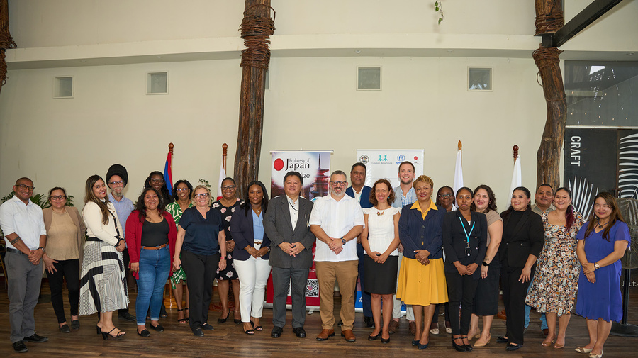 16 mujeres y 7 hombres con vestimenta formal posan para la foto en una sala de conferencias