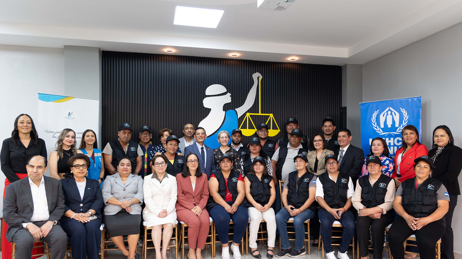 21 personas están de pie, detrás de 11 personas que están sentadas en sillas doradas