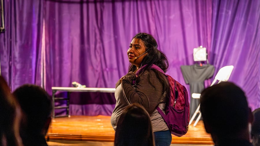Una mujer con una mochila roja en su espalda, en una puesta en escena en un teatro