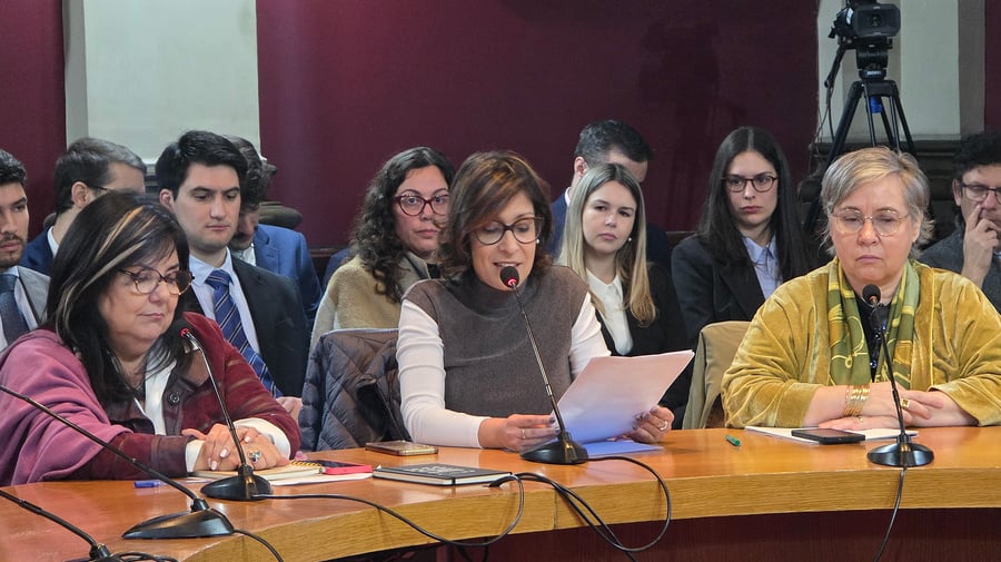 Tres mujeres con vestimenta formal y que portan anteojos las tres, están sobre una mesa con micrófonos