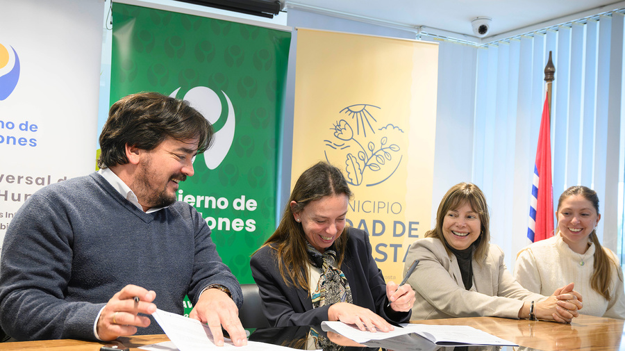 Un hombre y tres mujeres sonríen mientras firman documentos