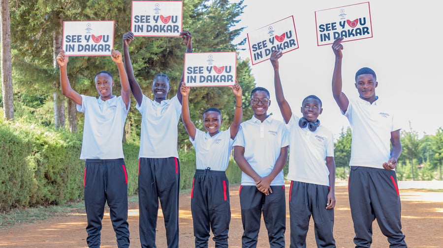 Seis jóvenes sonrientes que visten ropa deportiva, sostienen carteles que dicen "nos vemos en Dakar"