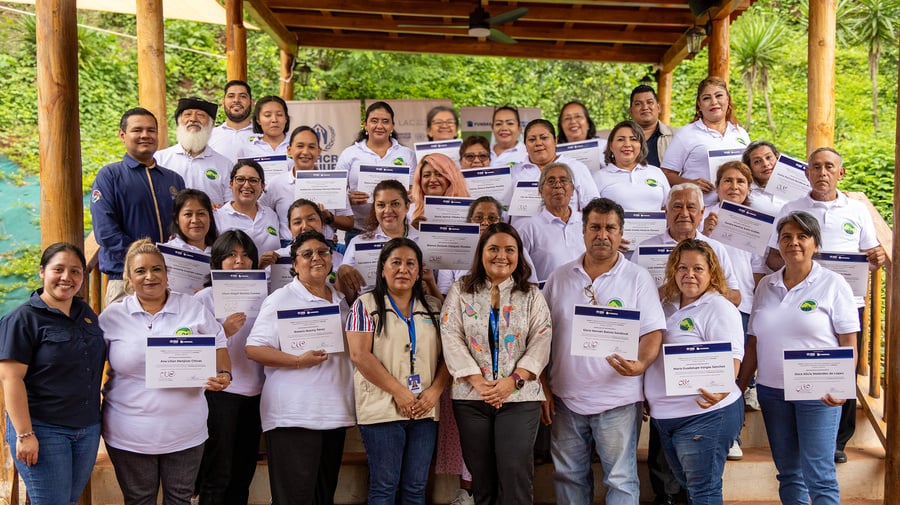 Un grupo de 26 mujeres y ocho hombres posan de pie en una escalera acomodados en fila, la mayoría sostiene un diploma en la mano