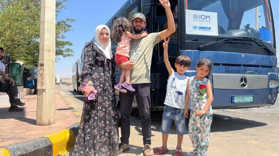 Un hombre, una mujer con sus dos niñas y un niño, posan para la foto de pie frente a un autobús de pasajeros