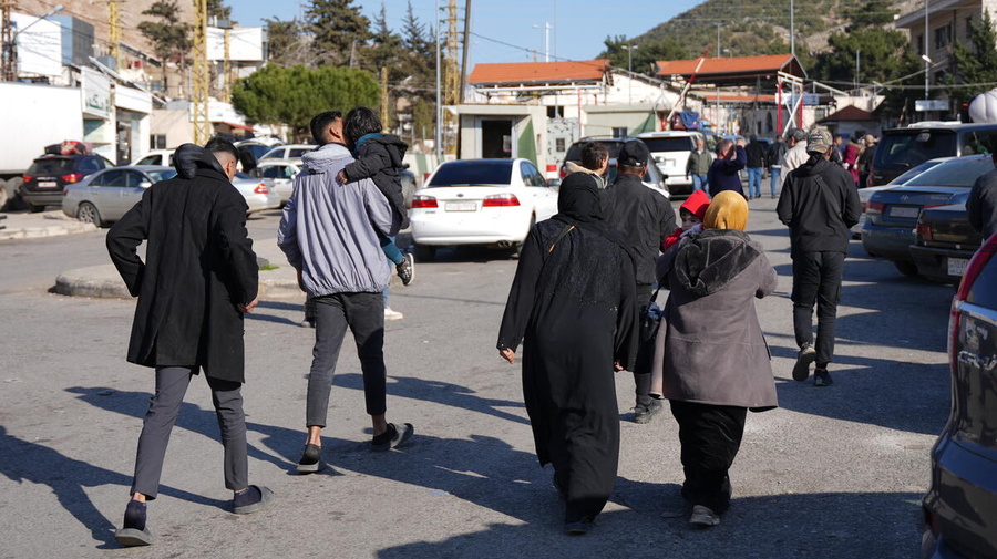 Un grupo de personas con ropa invernal caminando en una calle fotografiados de espaldas.