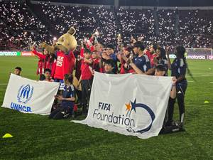 Decenas de niñas y niños reunidos al centro de una cancha de fútbol posan pasa la foto con uniformes deportivos