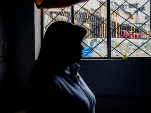 Una mujer fotografiada de perfil y contraluz mira a través de una ventana.
